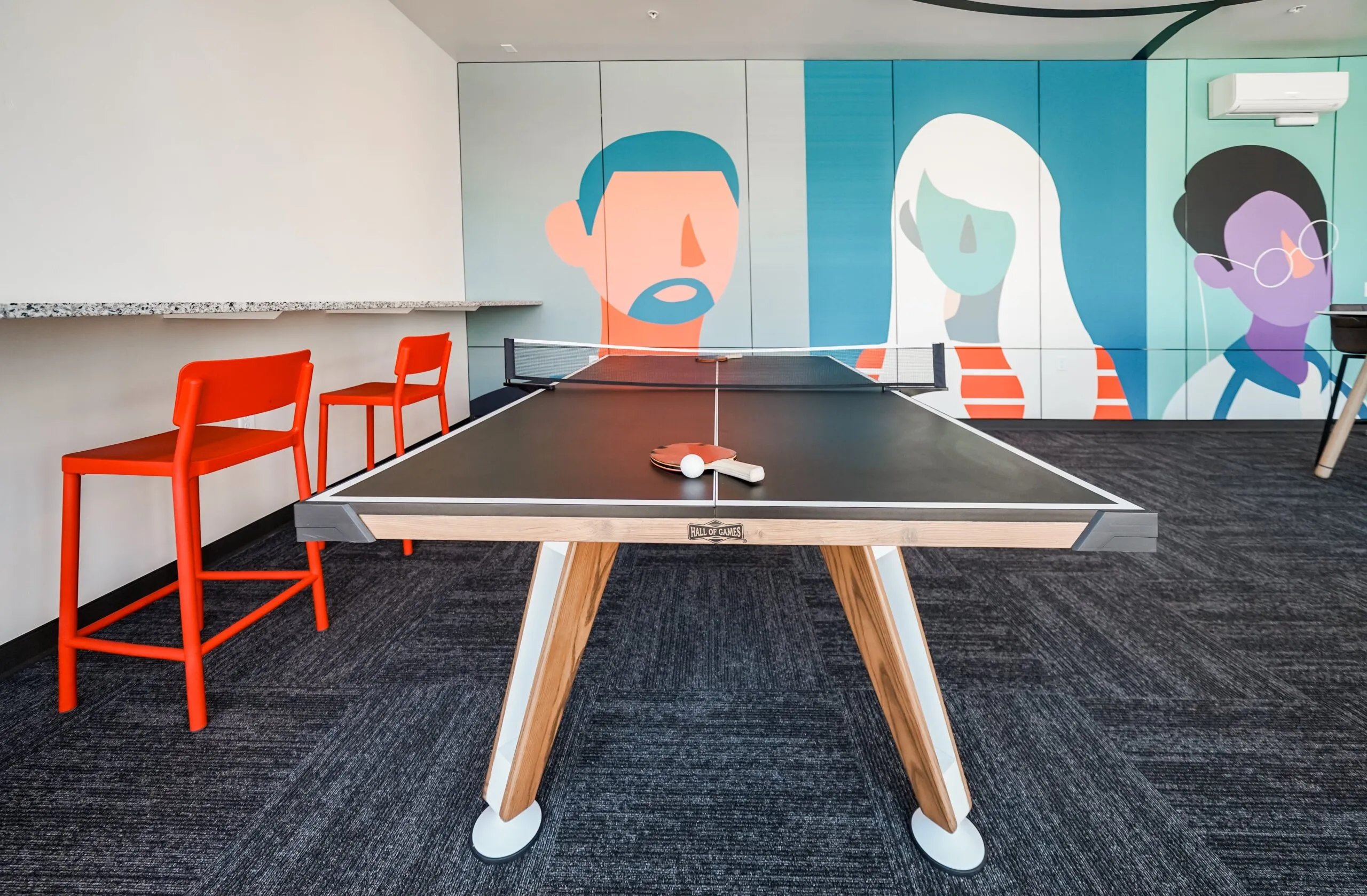 Ping pong table in the resident game room at aQui355 apartments in Salt Lake City, UT, with colorful murals and bar stools in the background.