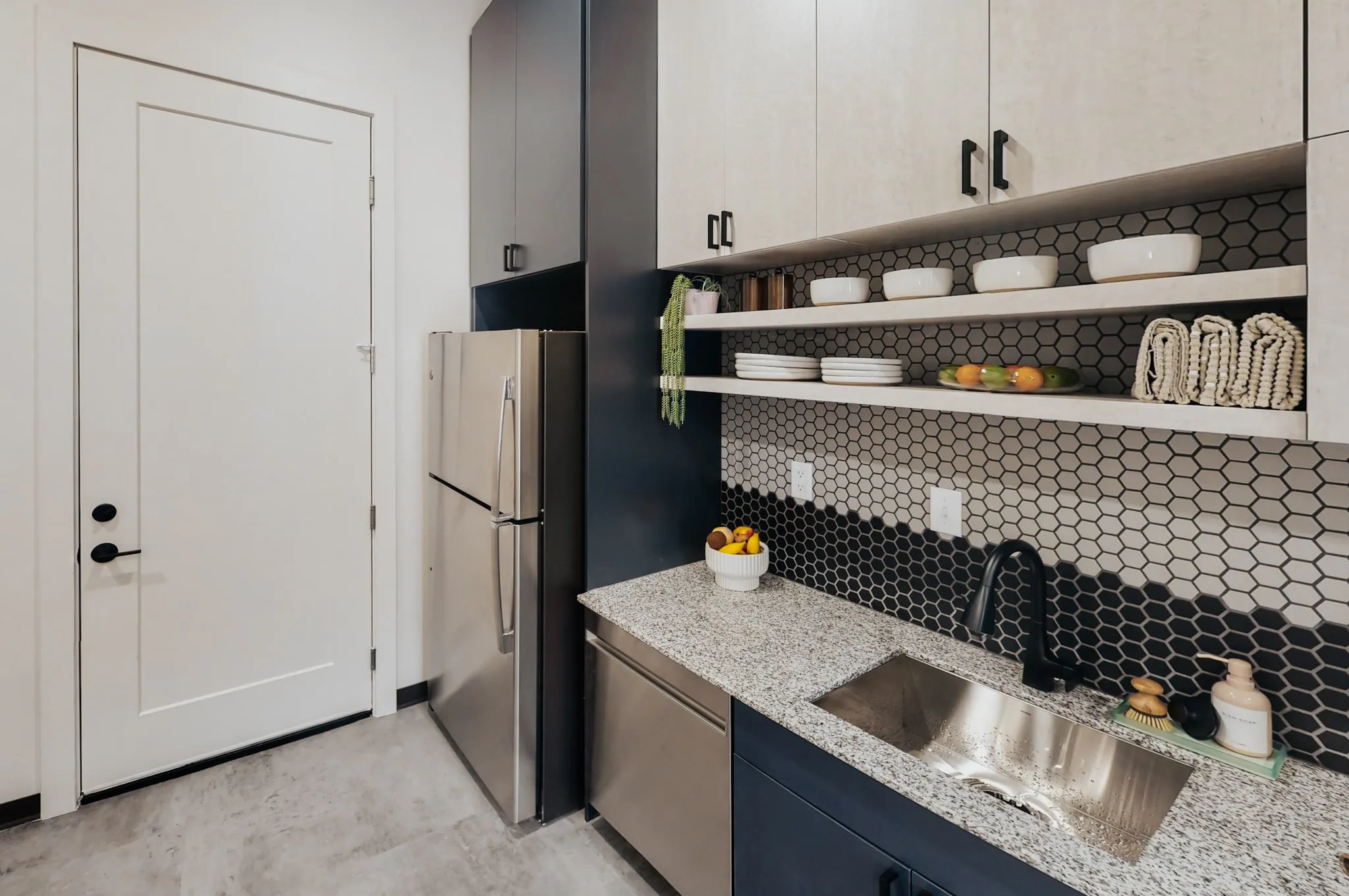 Detail of a modern kitchen at aQui355 apartments in Salt Lake City, Utah, highlighting open shelving, granite countertops, and a black hexagonal backsplash.
