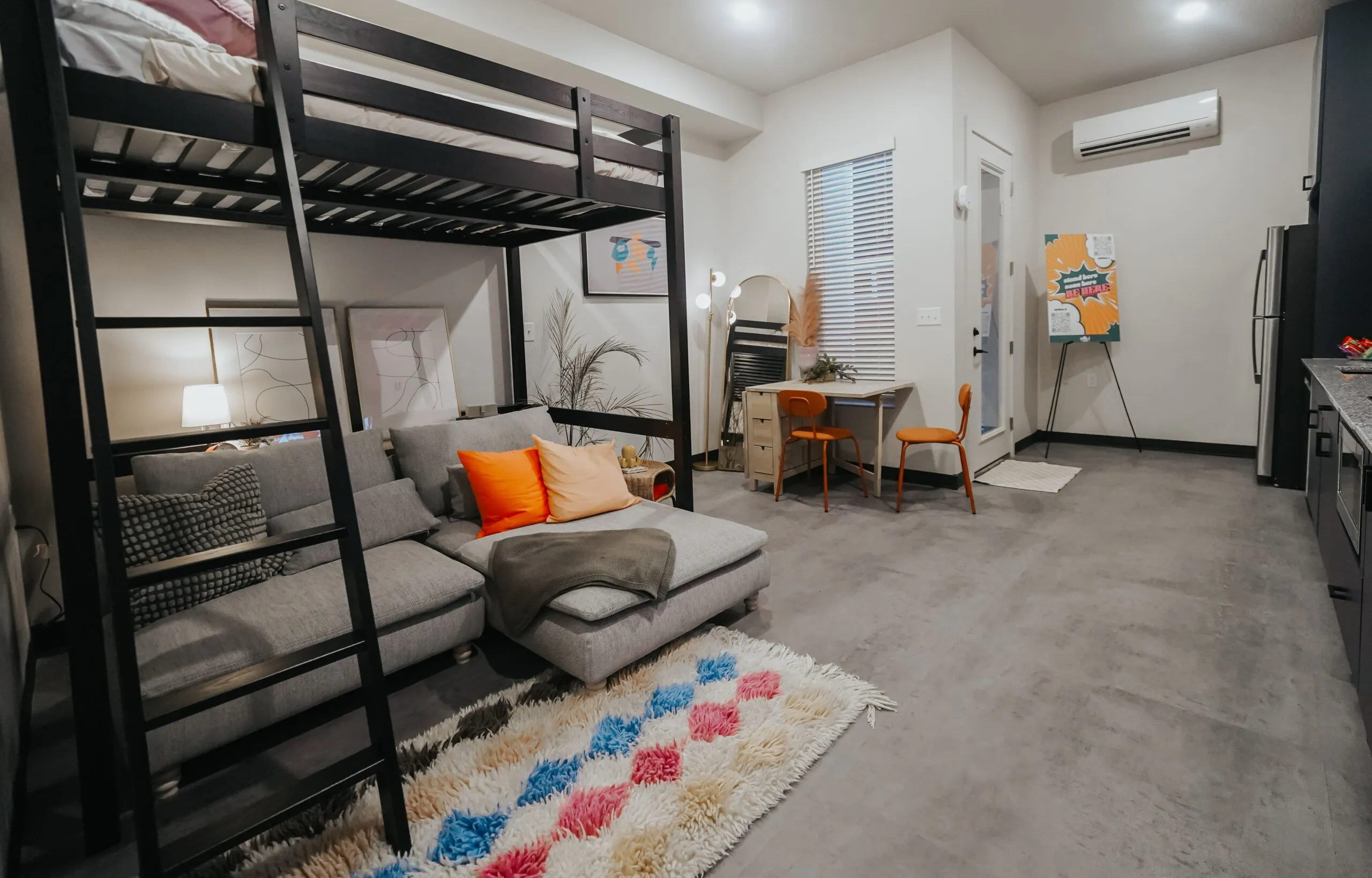 Loft-style apartment interior at aQui355 in Salt Lake City, UT, featuring a bunk bed, living area with sofa, and a compact kitchen.