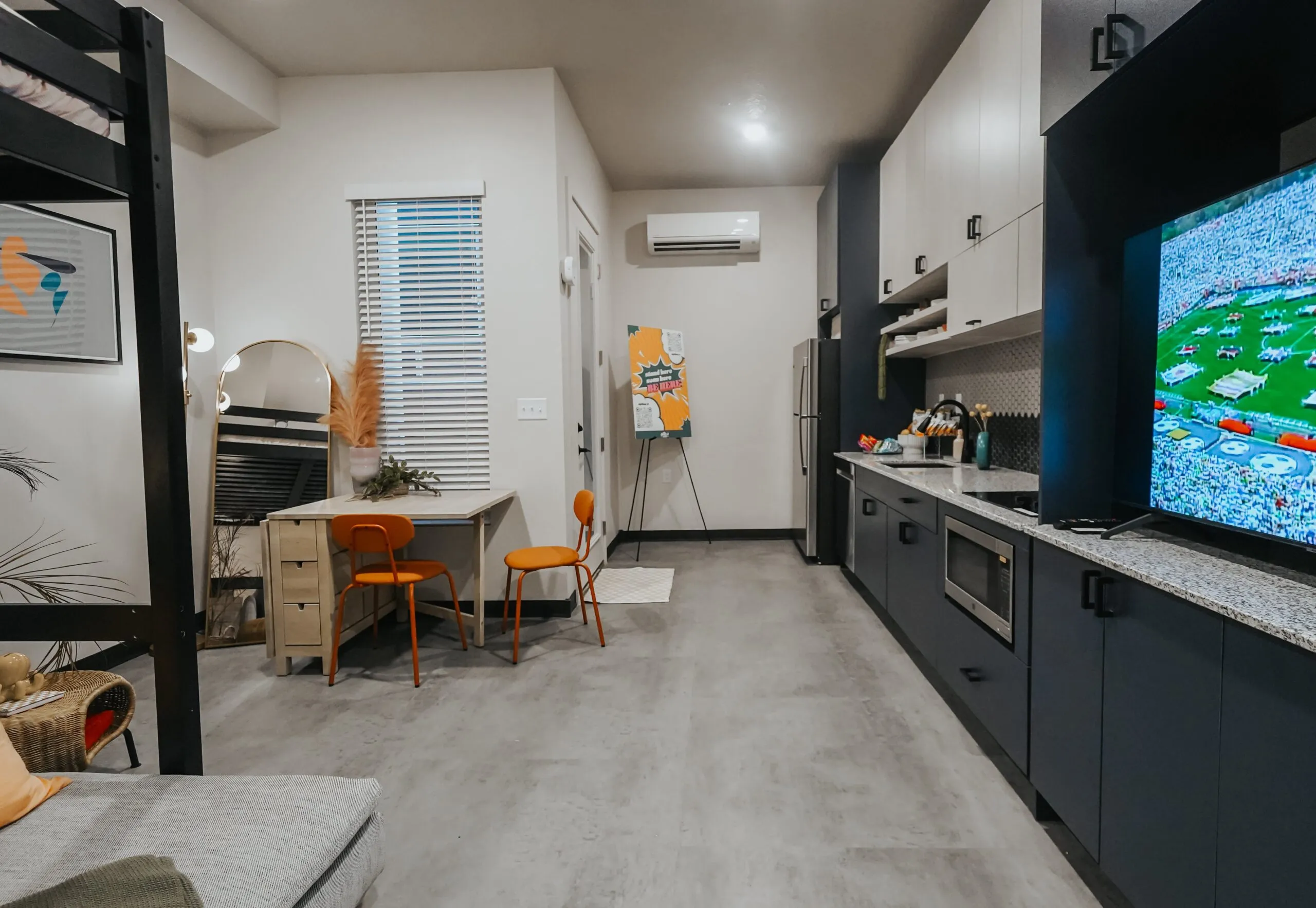 View of a compact kitchen and living area in an aQui355 apartment unit, Salt Lake City, UT, featuring a loft bed, dining table, and TV.