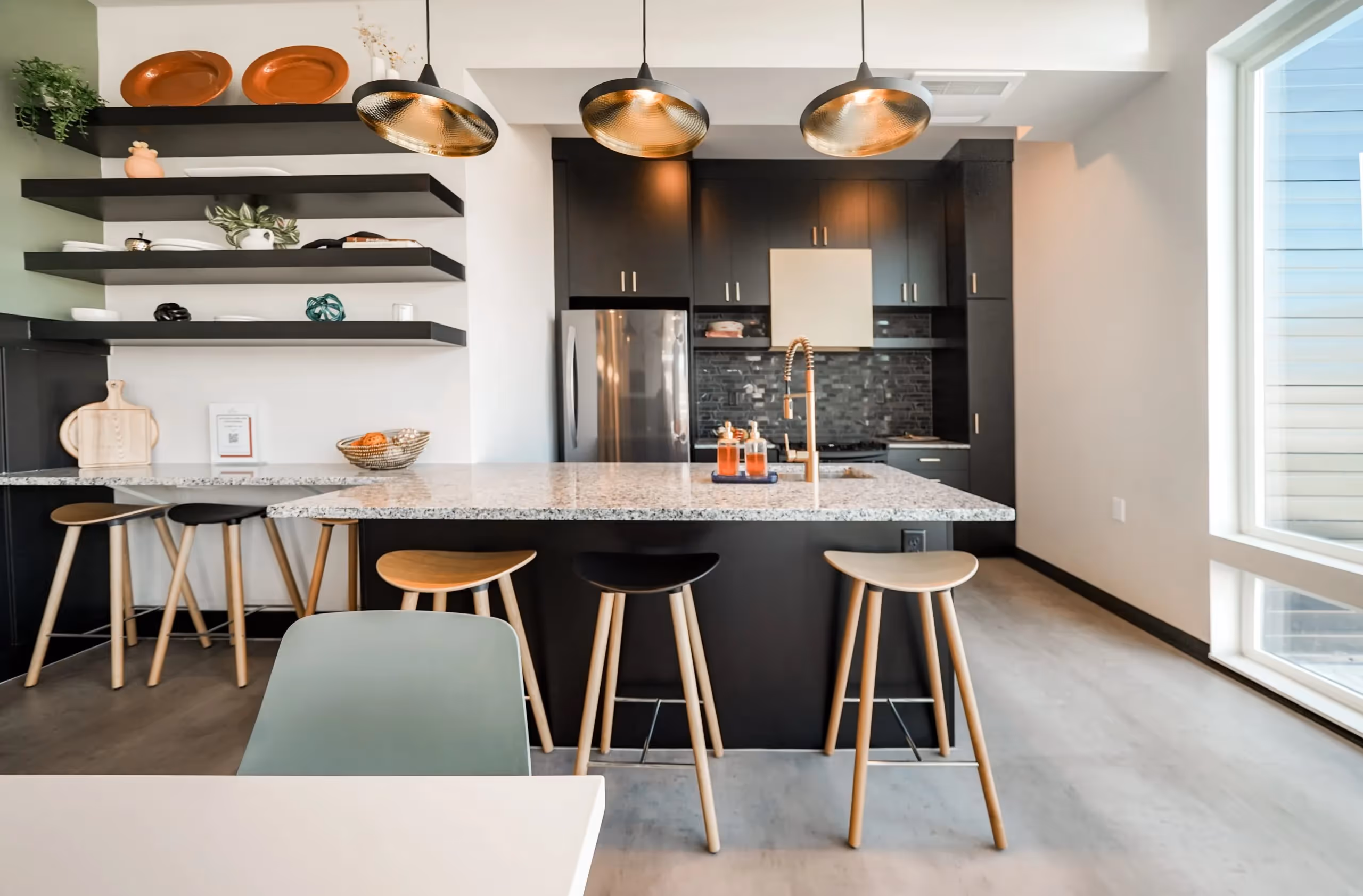 Modern kitchen with a large island, granite countertops, bar stools, black cabinetry, and floating shelves at aQui355 apartments in Salt Lake City, UT.
