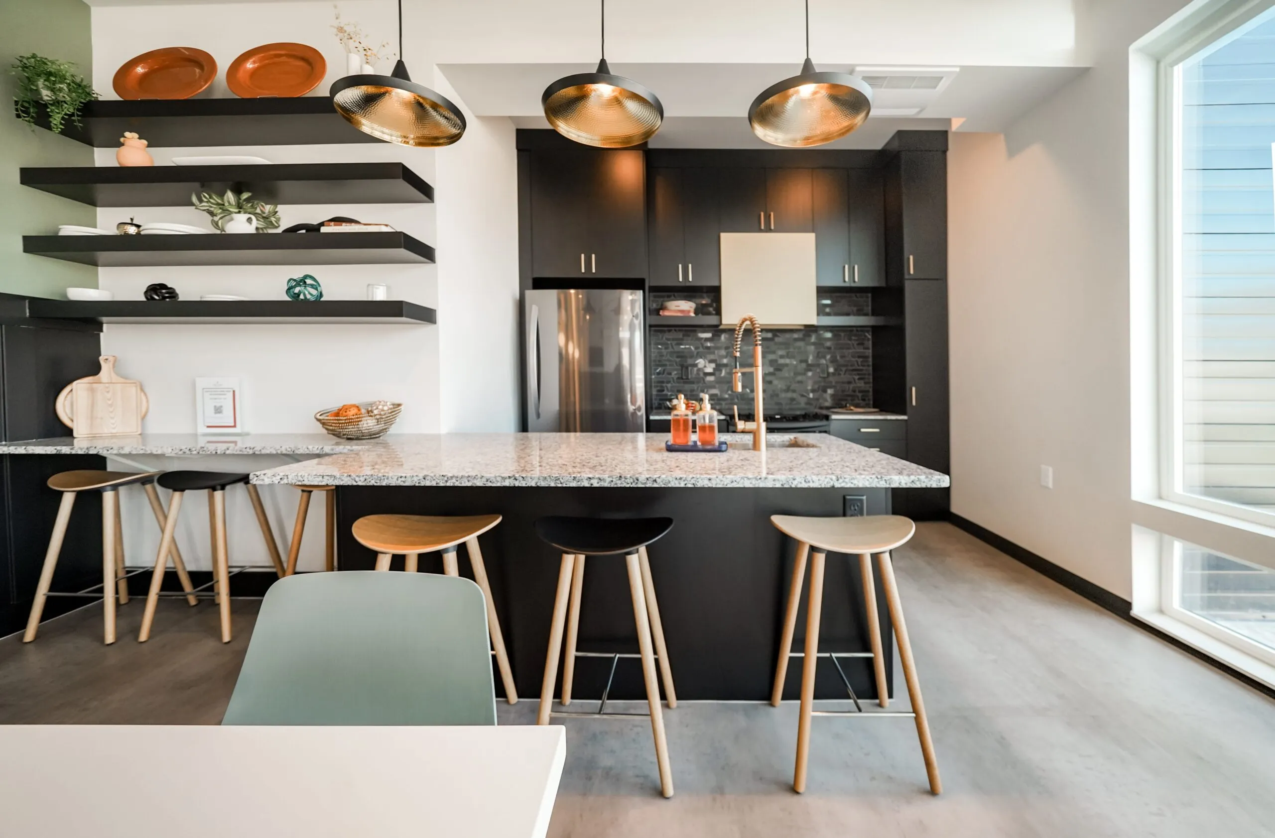 Modern kitchen with a large island, granite countertops, bar stools, black cabinetry, and floating shelves at aQui355 apartments in Salt Lake City, UT.