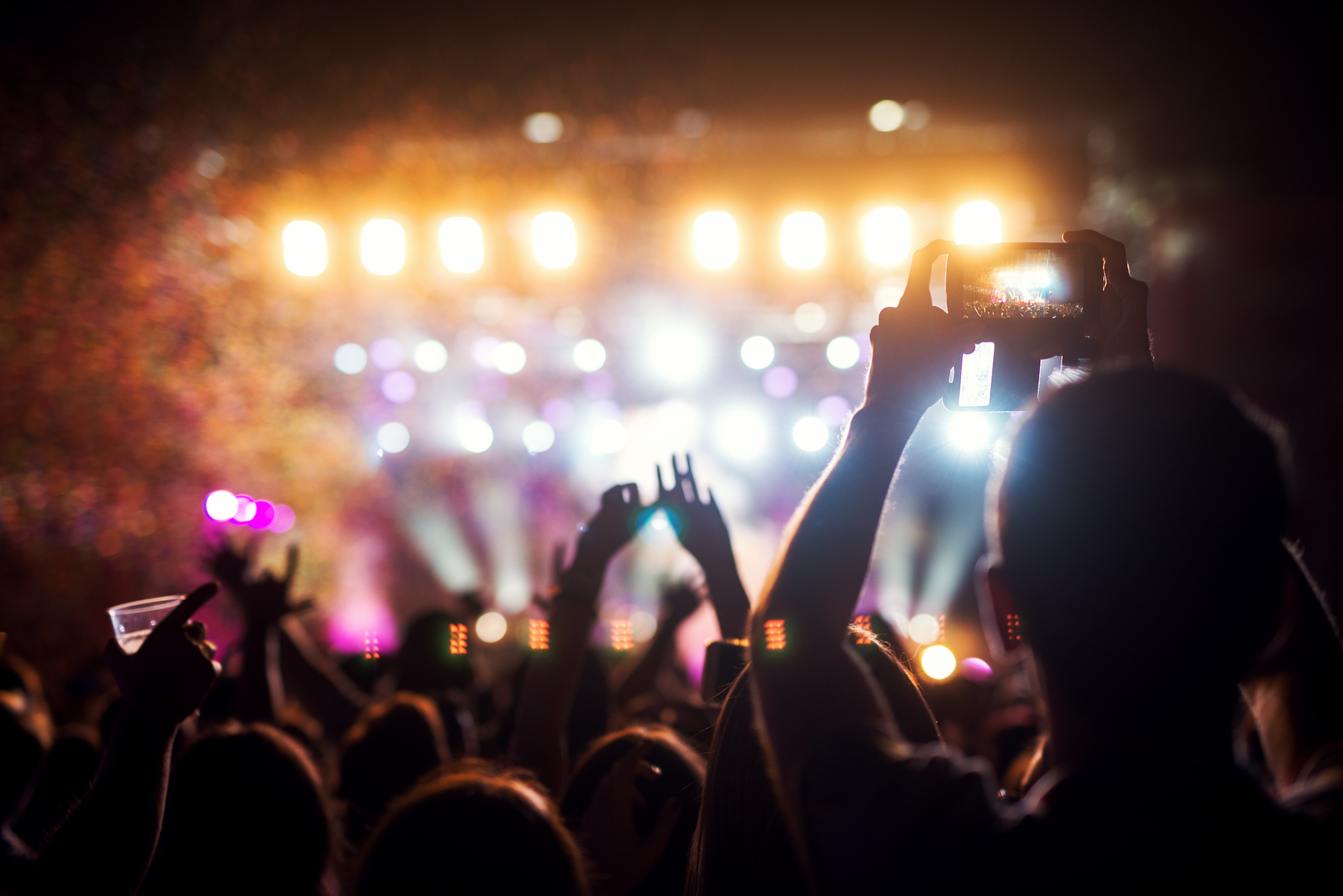 Concert crowd with hands raised and phones recording, lights on stage in the background, representing the vibrant entertainment scene and local events near aQui355 apartments in Salt Lake City, Utah.