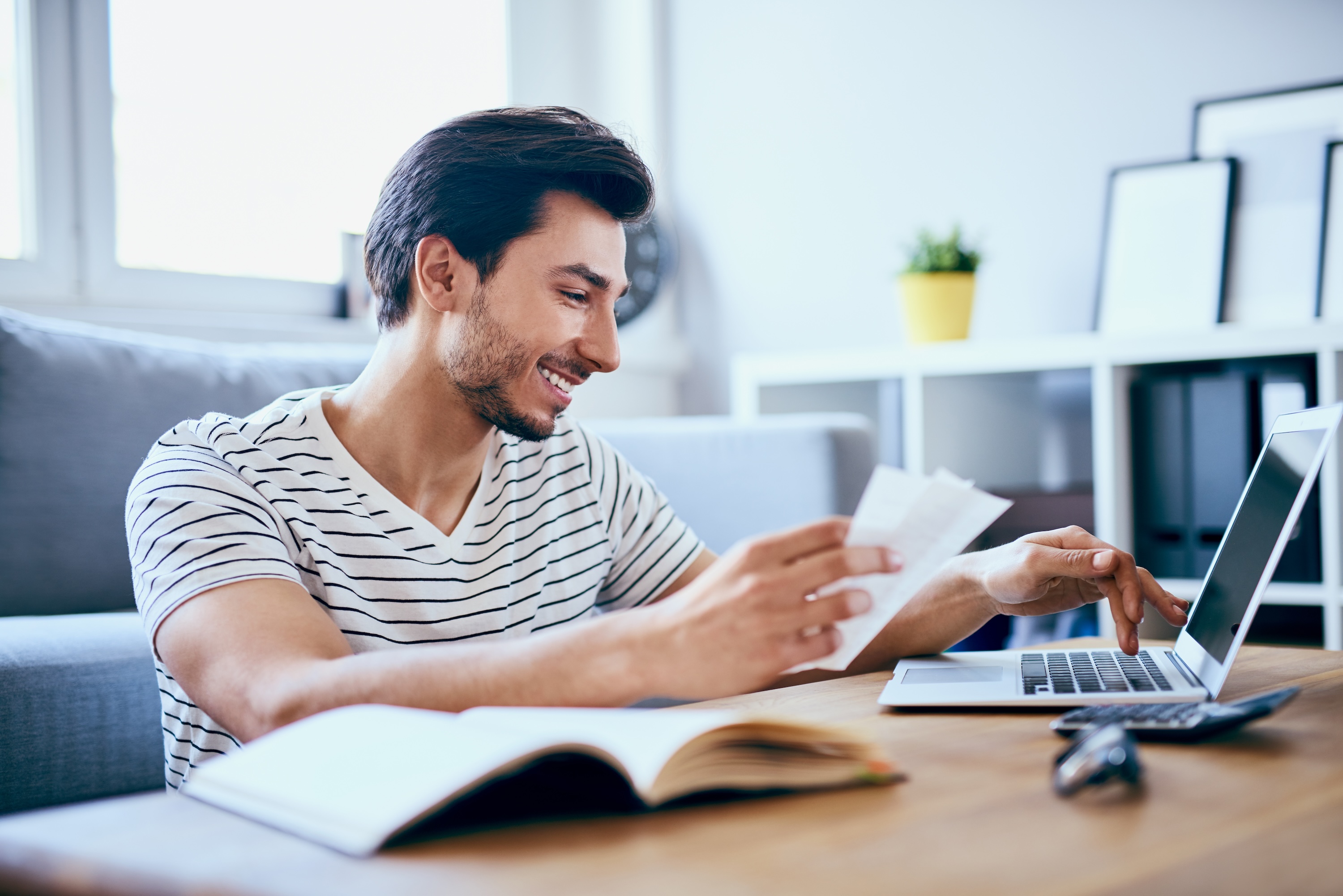 A smiling resident reviewing paperwork and using a laptop in a living room at aqui355 in Salt Lake City, UT.