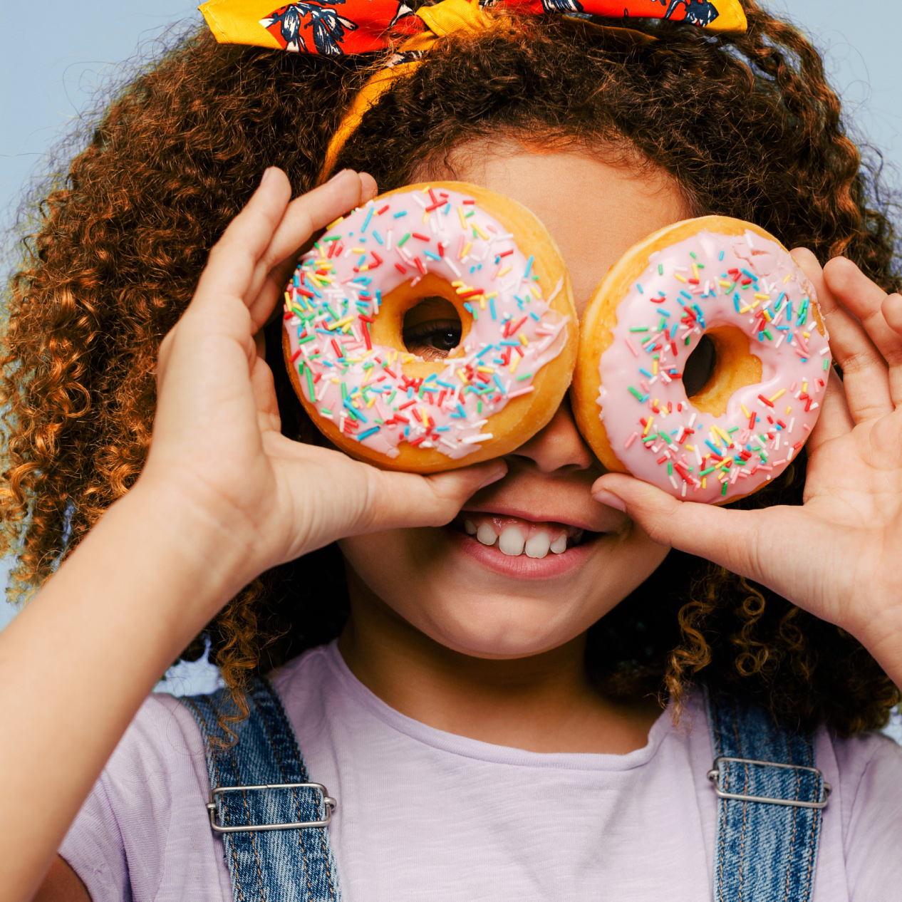 Image of young girl holding two donuts up to her eyes and smiling