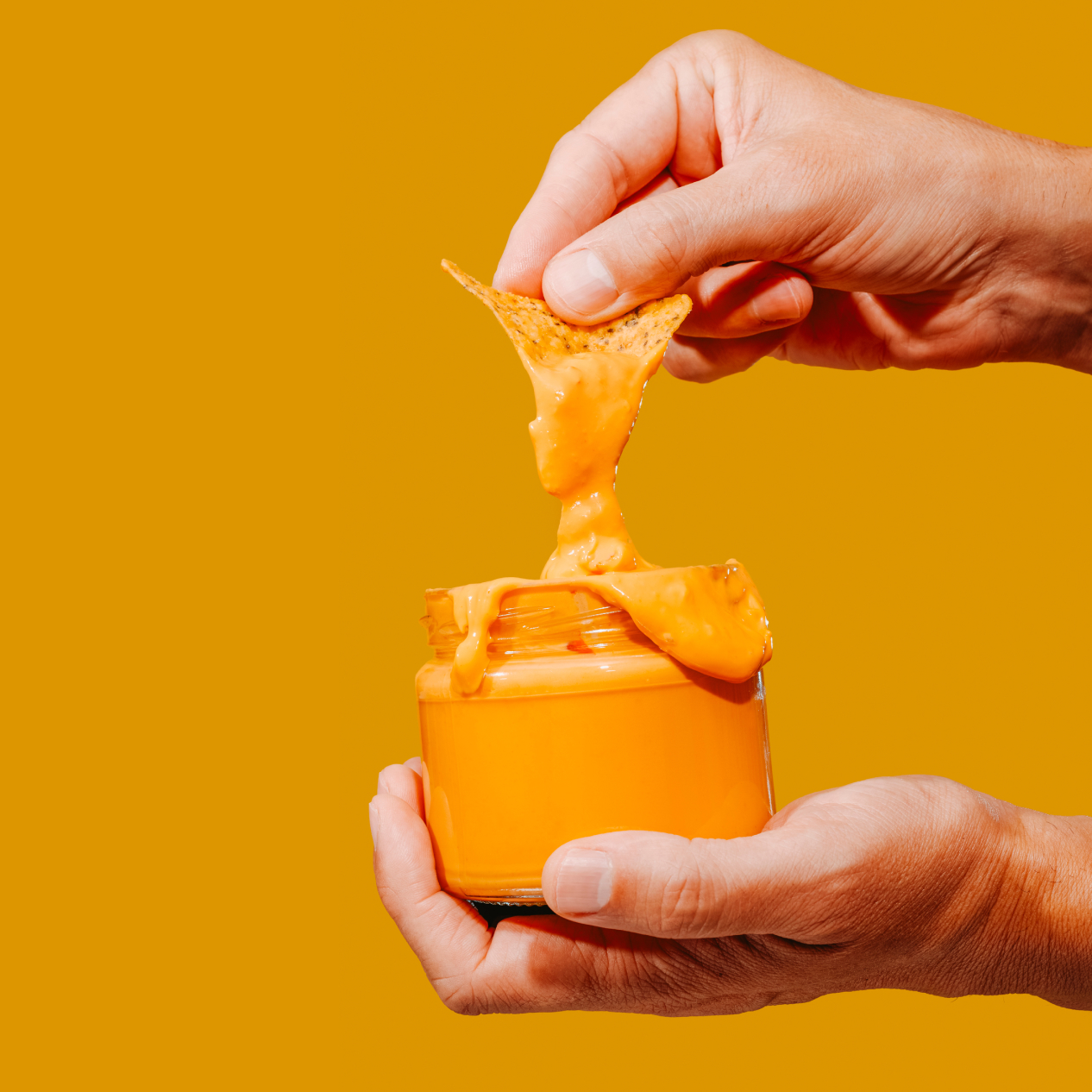 Image of a person dipping a tortilla chip in a cheese dip