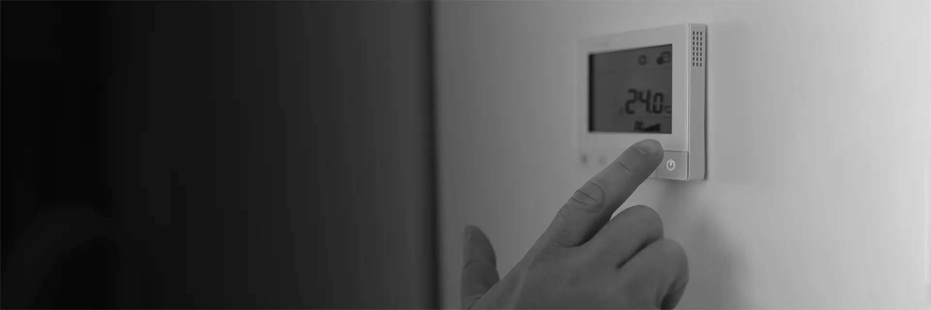 A hand pressing the power button on a wall-mounted digital thermostat displaying 24.0 degrees.
