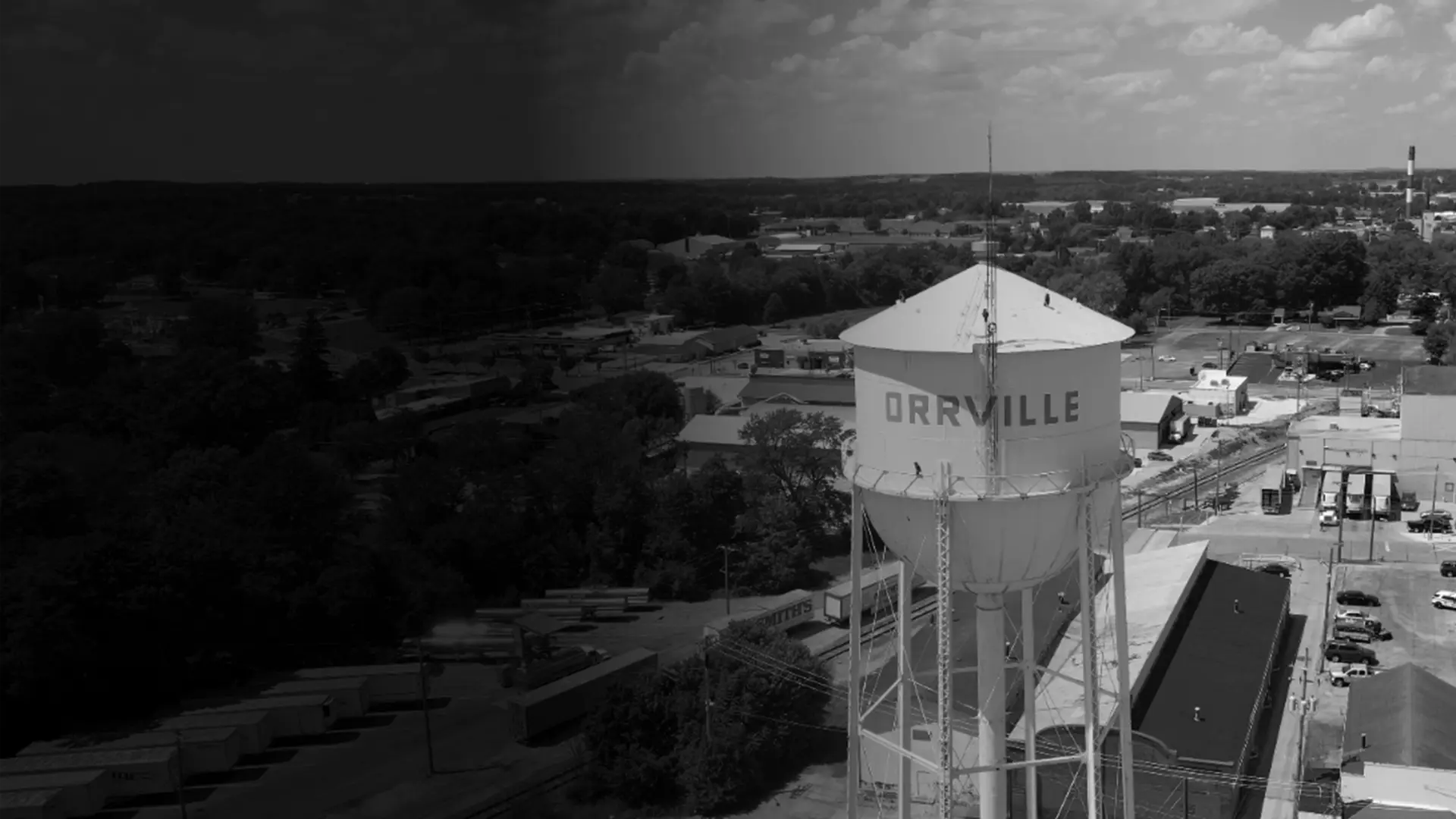 Historic courthouse building with a clock tower, flags, and surrounding trees in black and white.