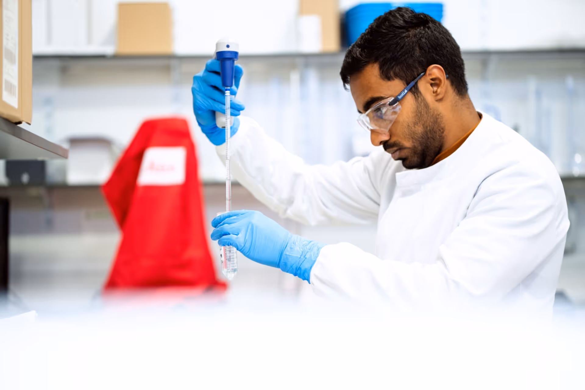 Scientist in a white lab coat and blue gloves using a pipette to transfer liquid in a laboratory.