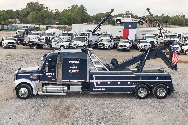 Heavy-duty Texas Towing truck in foreground, surrounded by a large fleet of tow trucks with Texas and American flags prominently displayed.
