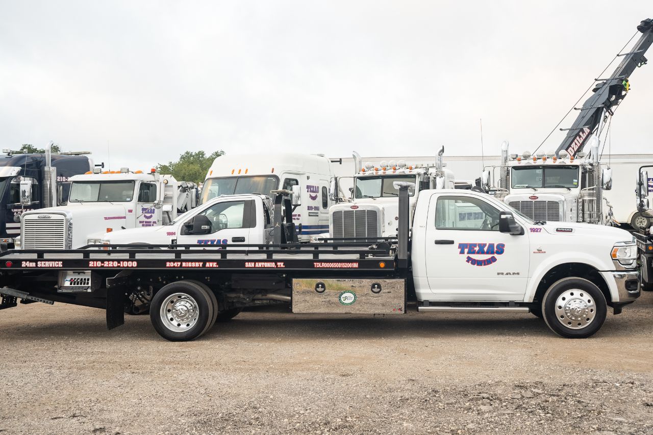 Tow truck operator secures equipment on flatbed Texas Towing vehicle in parking lot, surrounded by other tow trucks and trees