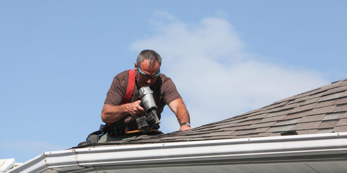 roofer with nail gun installing shingles