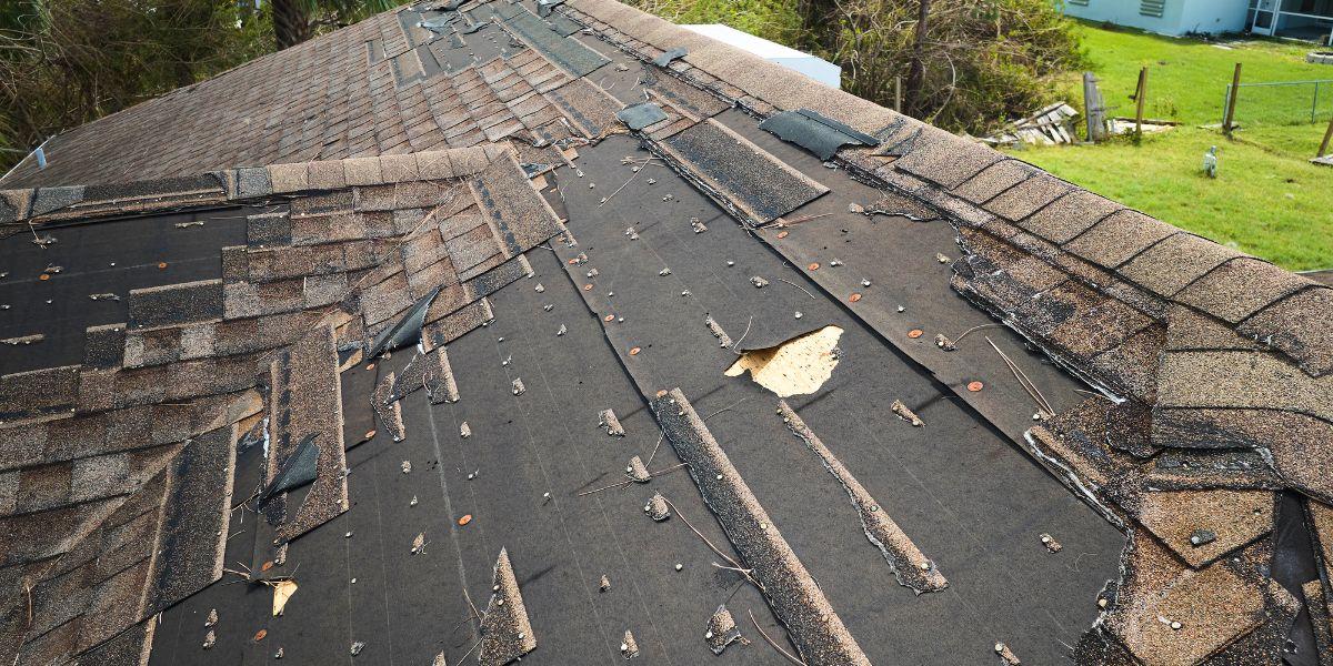 Severely damaged asphalt shingle roof with missing shingles and exposed underlayment illustrating when the 50% roof replacement rule may favor replacing instead of repairing.
