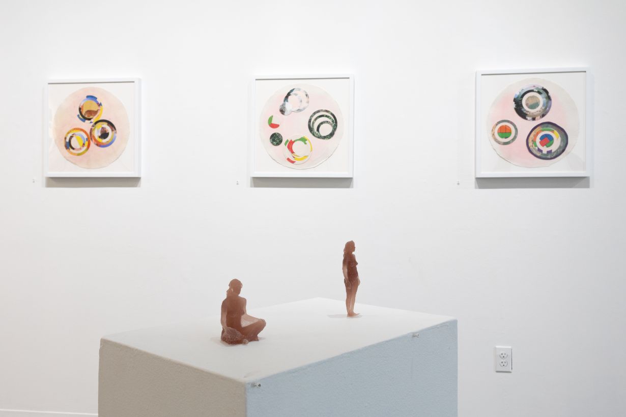 Group of five people seated in a gallery with framed and round artworks on the white walls, engaged in a discussion.
