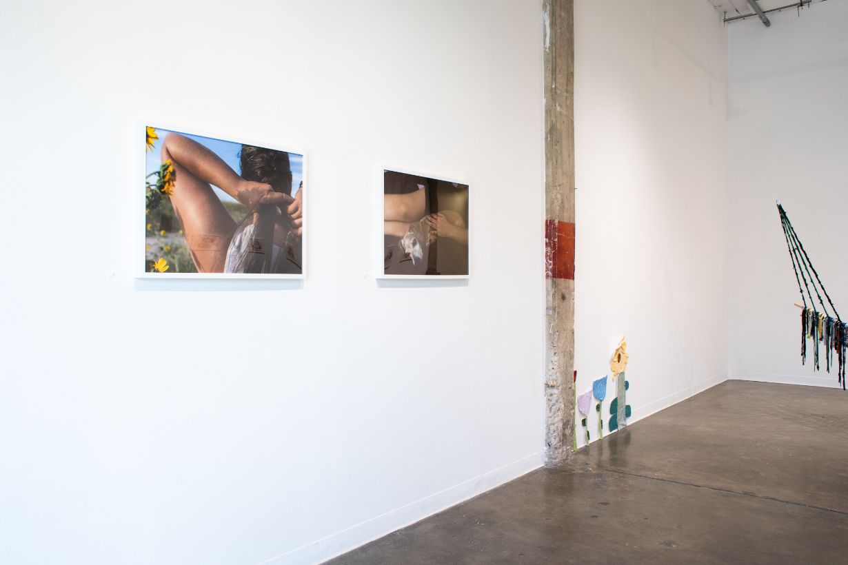 Art gallery wall featuring various framed photos including a large lake reflection with a circular mirror, a hand print, abstract images, and two figures on a dark ground under a twilight sky.