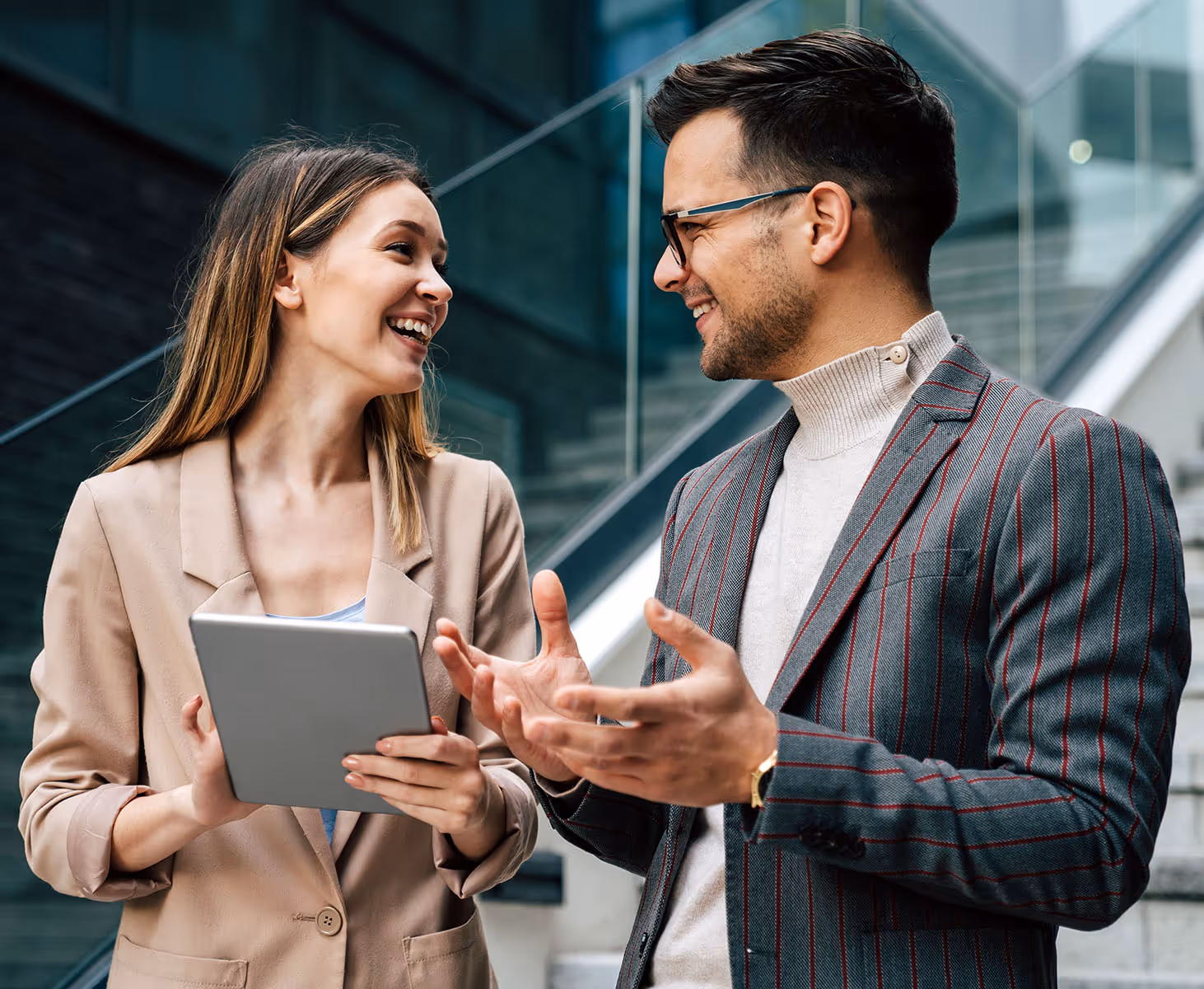 Two business professionals smiling and discussing while looking at a tablet in an office setting.