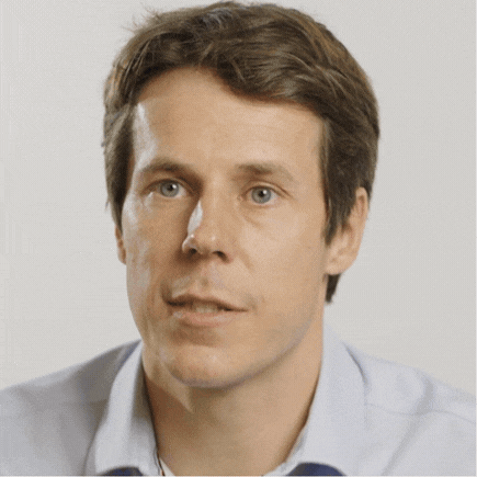 Man with short brown hair and blue eyes speaking while wearing a light blue collared shirt.
