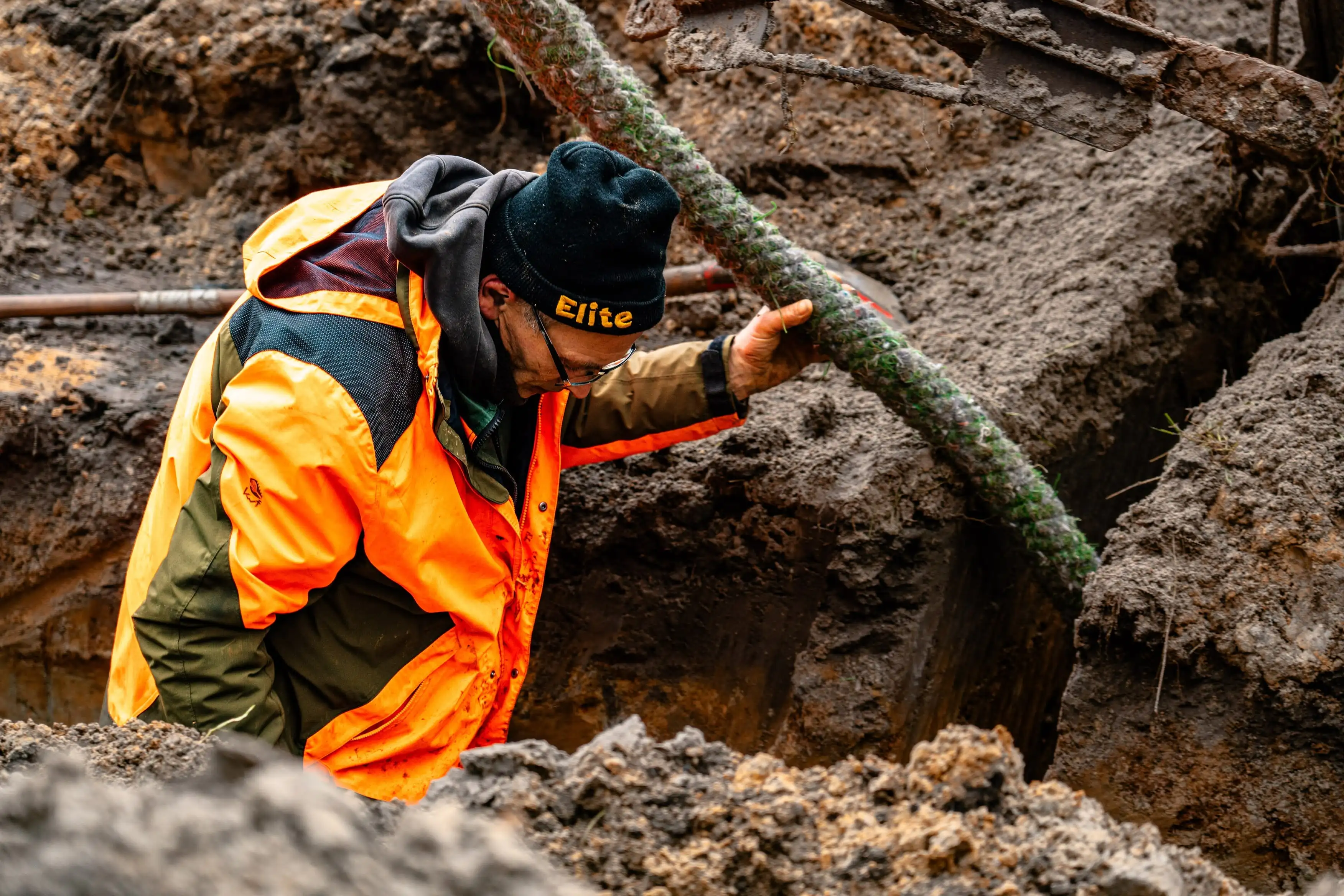 A man in an orange jacket is working on a pipe.