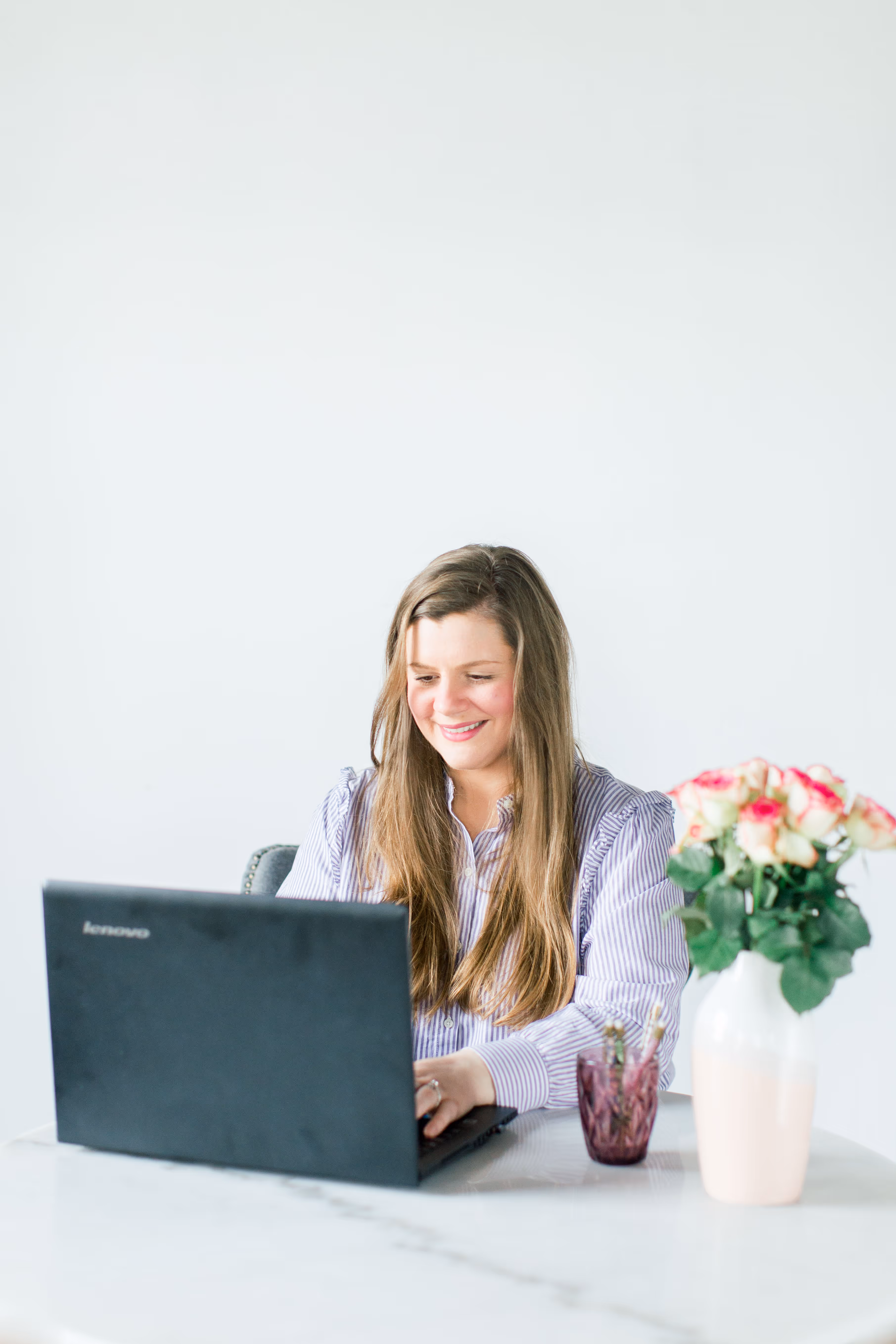 Rachael Lantz, owner of Happy Sparrow Marketing, sitting at a table with a laptop, smiling with a vase of flowers beside her