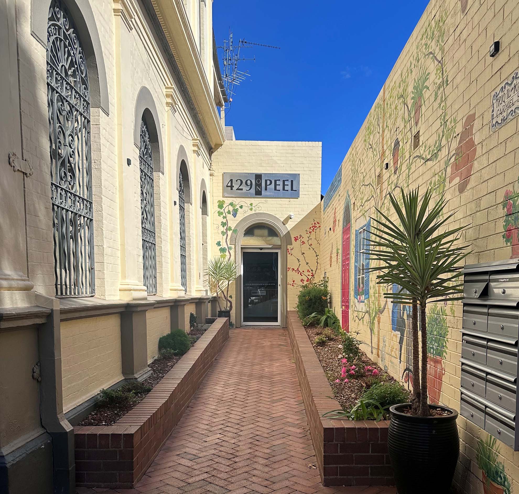 Narrow brick walkway between buildings with arched windows and mural on right wall at 429 Peel.