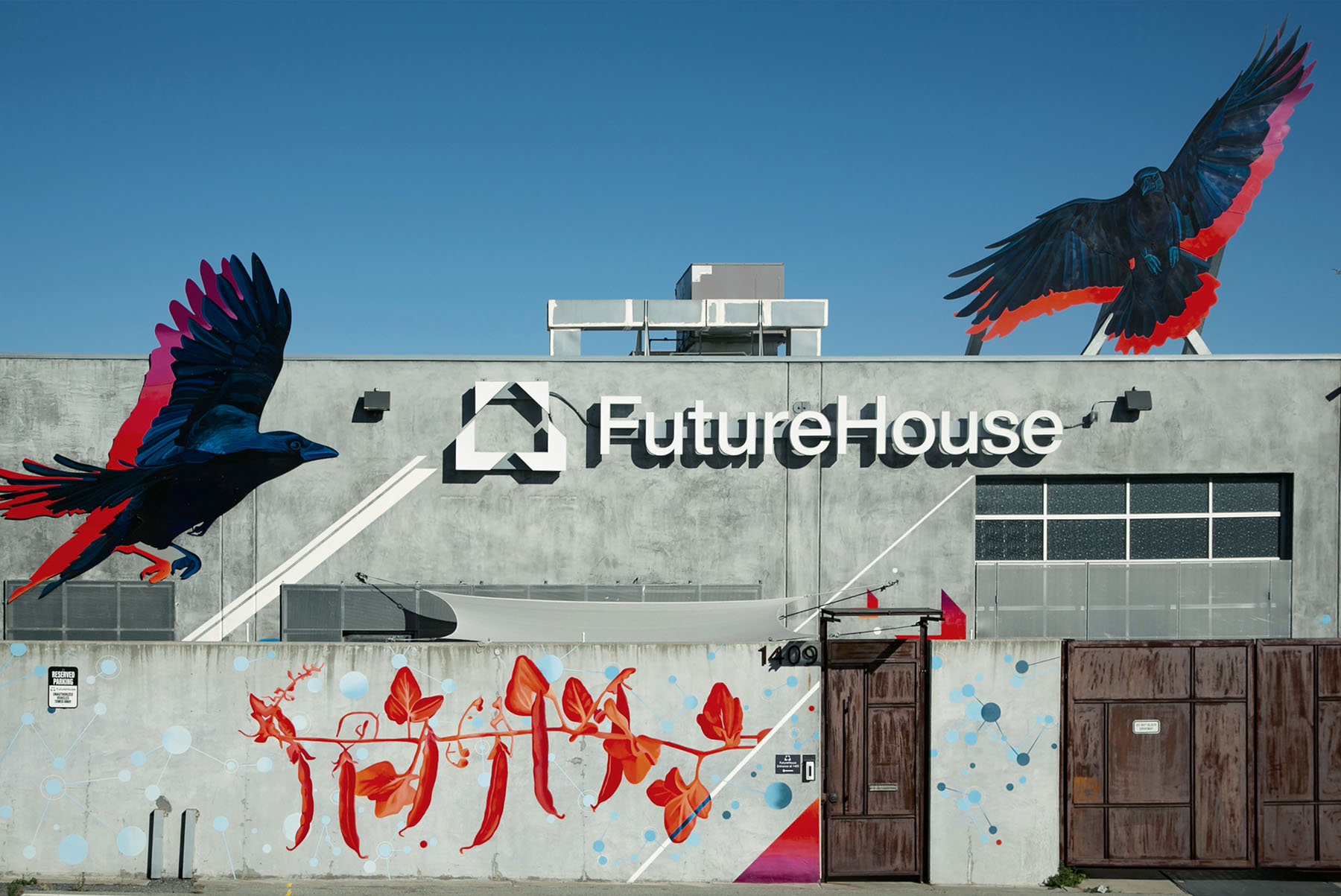 Gray industrial building with FutureHouse sign and logo, decorated with large murals of black and red birds and red chili pepper artwork on the wall.