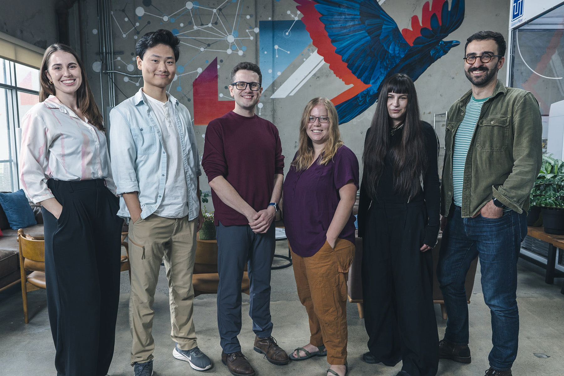 Group of six FutureHouse Fellows standing indoors in front of a wall mural with a blue and red bird and geometric designs.