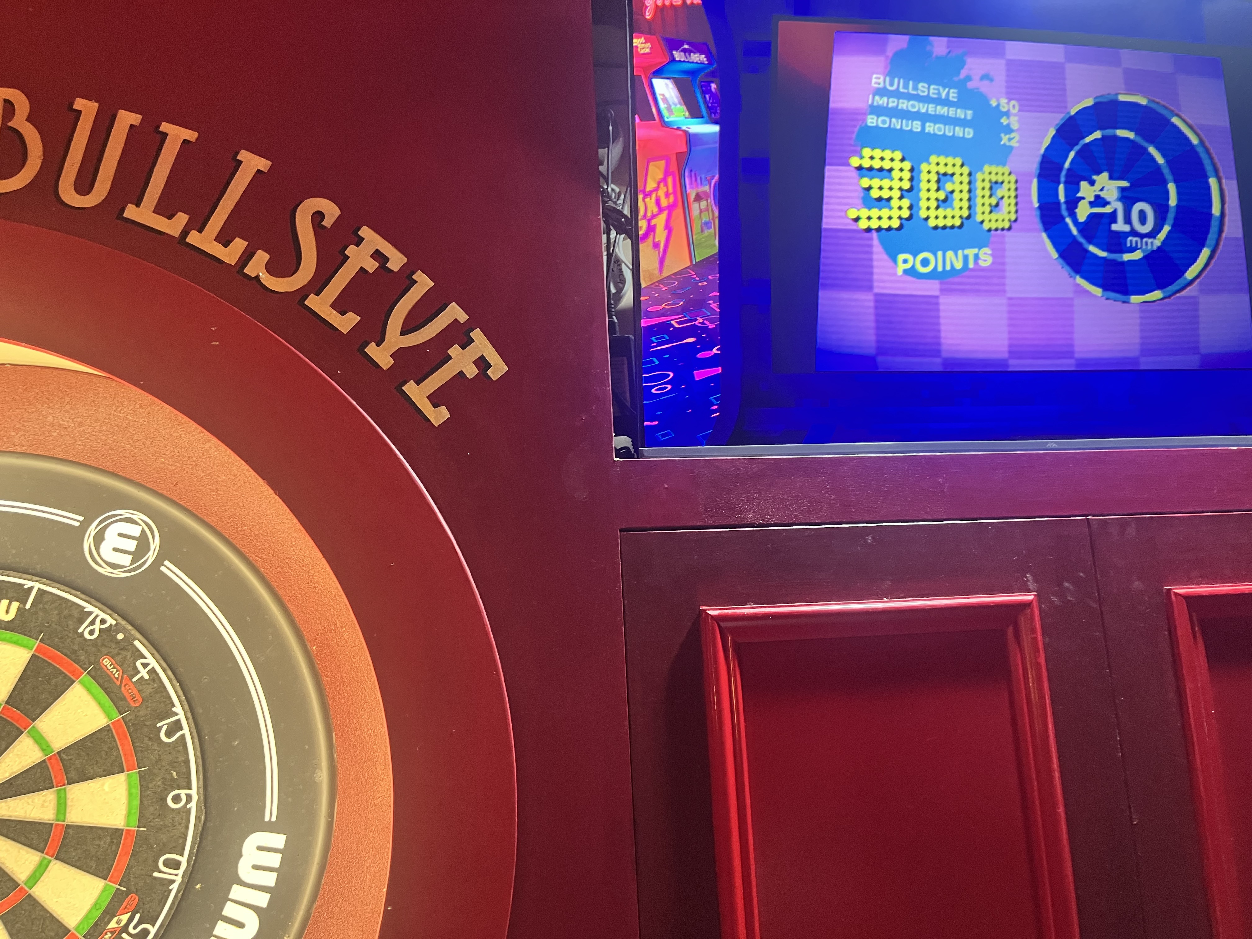 Electronic dartboard labeled Bullseye next to a screen displaying a score of 300 points and a target graphic.