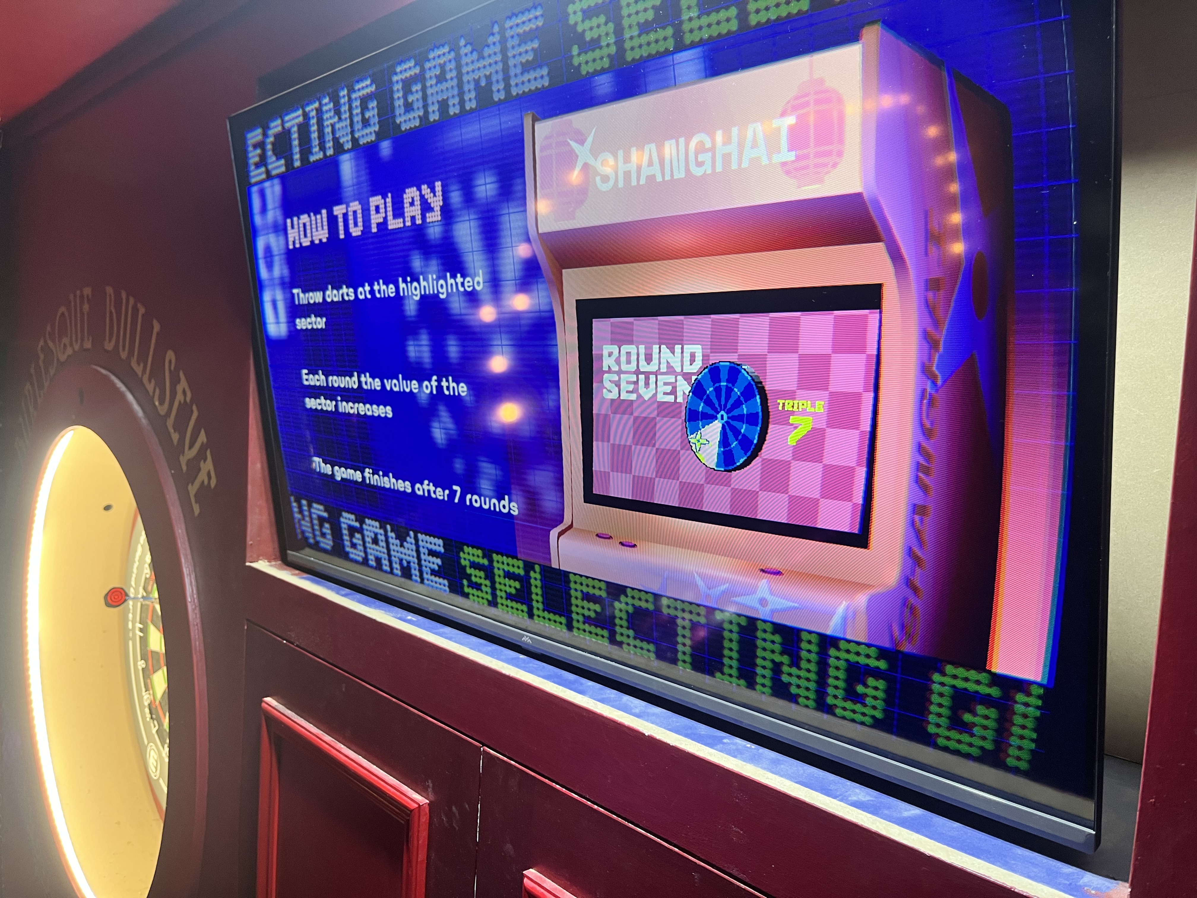 Electronic dartboard game with instructions on screen and a dart hitting the blue highlighted sector marked triple 7 in round seven.