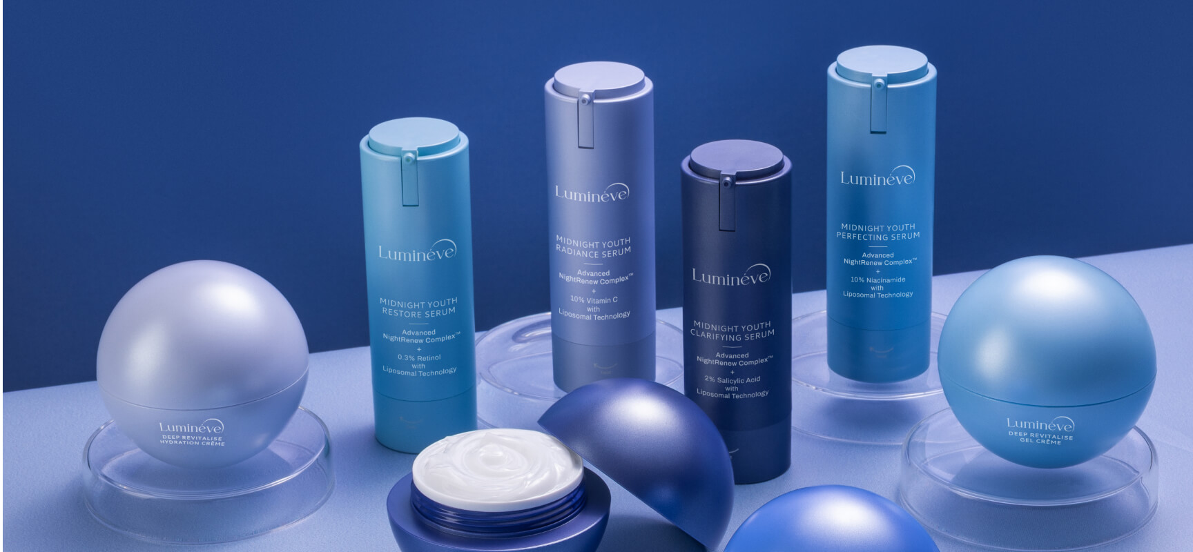 Seven Lumineve skincare products in blue and purple containers arranged on clear stands, including serums and hydration creams, with one container open showing white cream inside.
