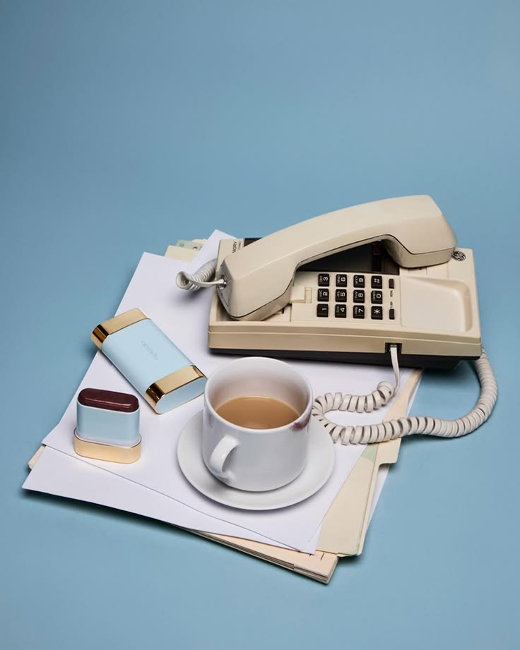 Vintage telephone placed beside a cup of coffee, notepad, and stationery items on a blue background.