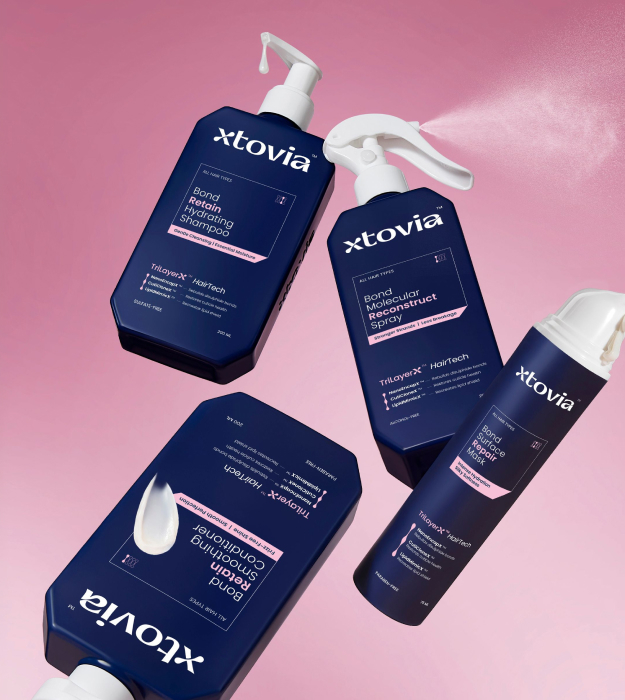 Four Xtovia bond repair haircare products including shampoo, conditioner, repair mask and reconstruct spray displayed on a clear acrylic shelf against a soft pink background.