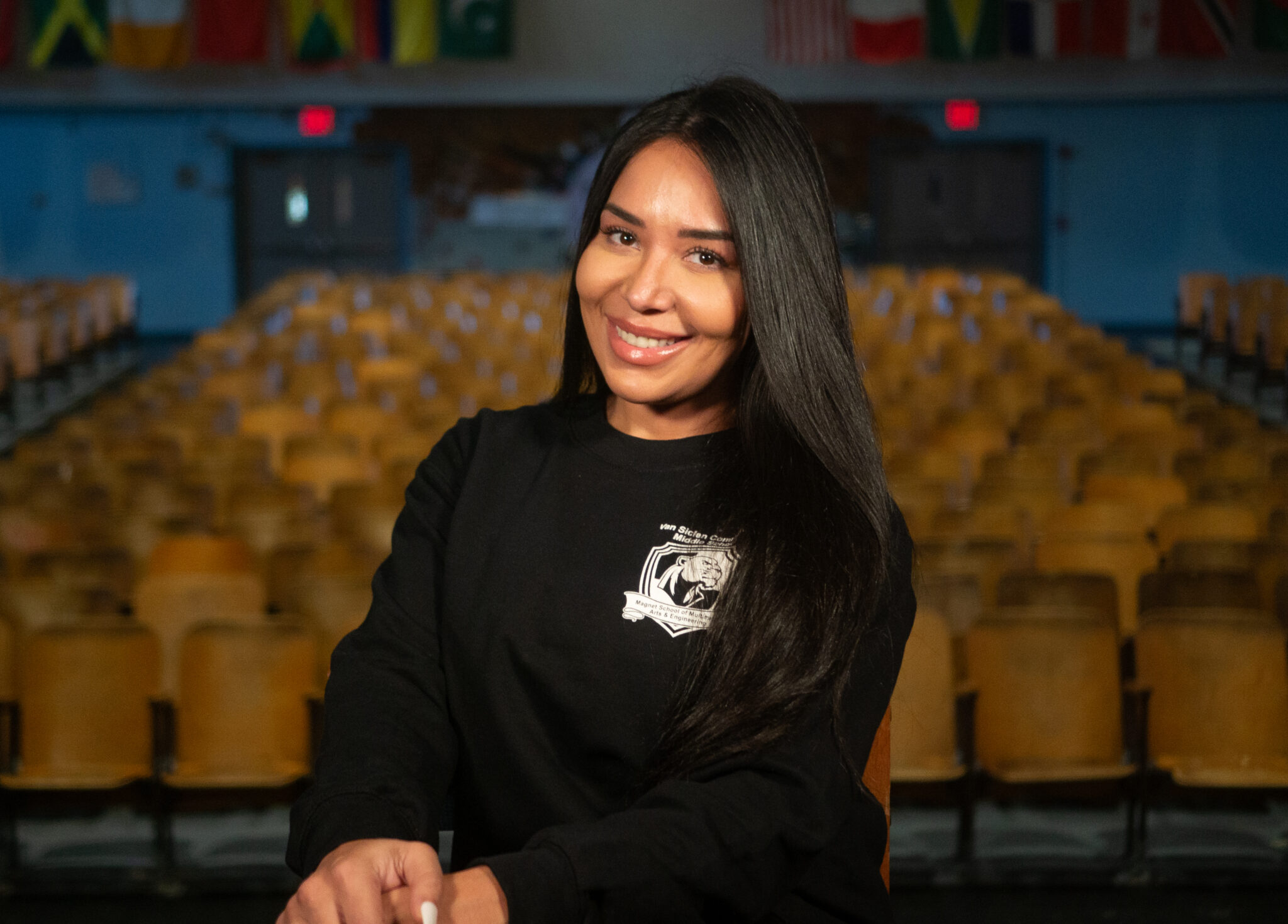 Smiling staff member seated in school auditorium with international flags