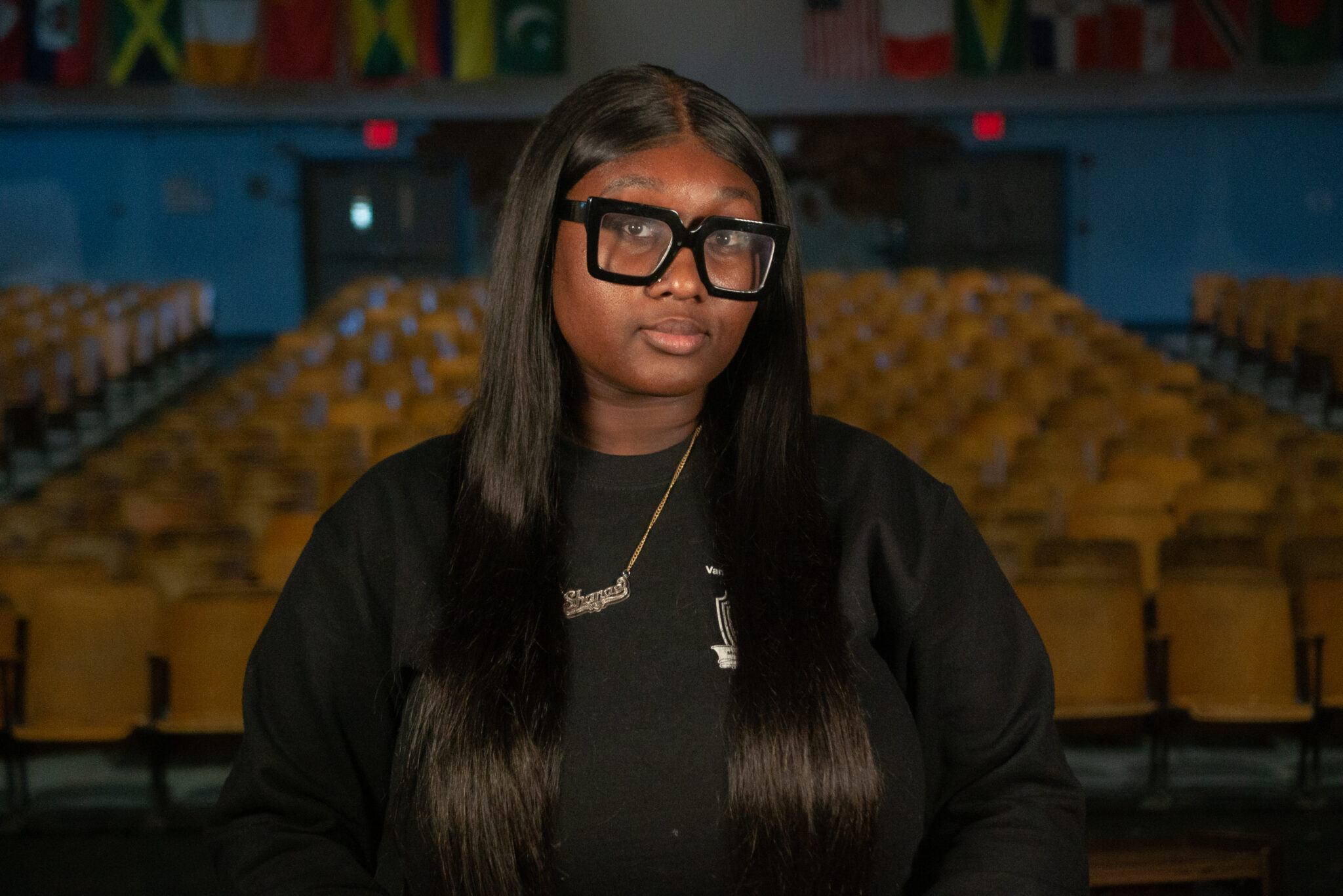 Student Shanae Phillips seated in school auditorium with international flags