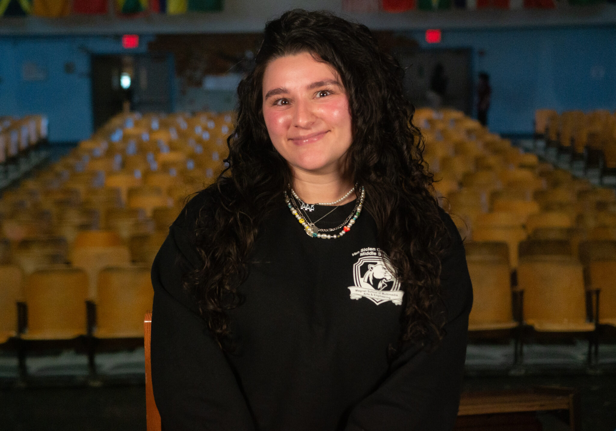 Student smiling in school auditorium wearing school sweatshirt