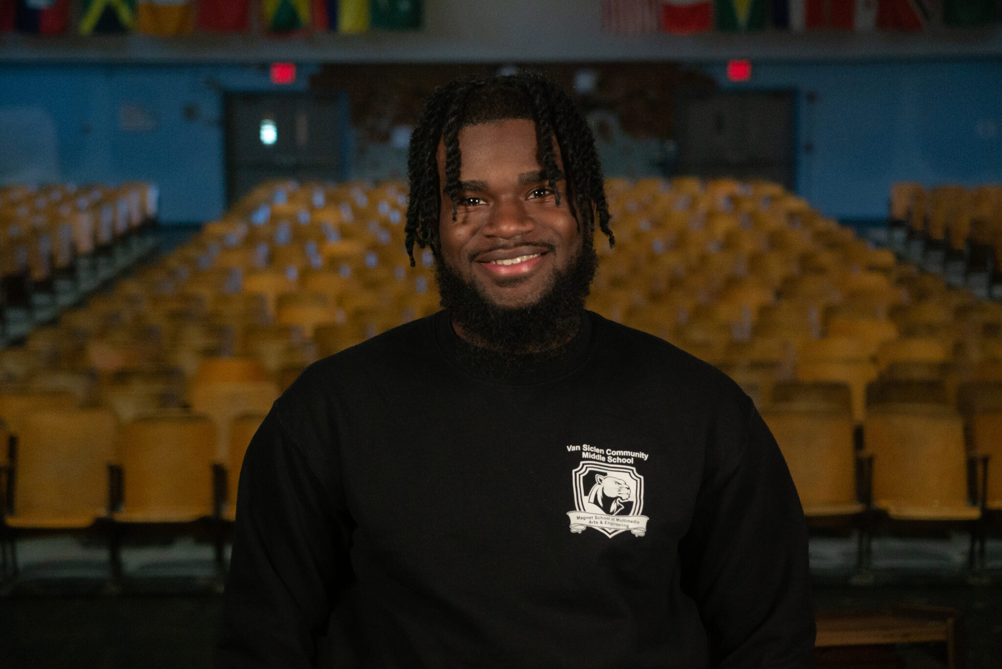 Smiling staff member wearing Van Siclen Community Middle School sweatshirt in auditorium