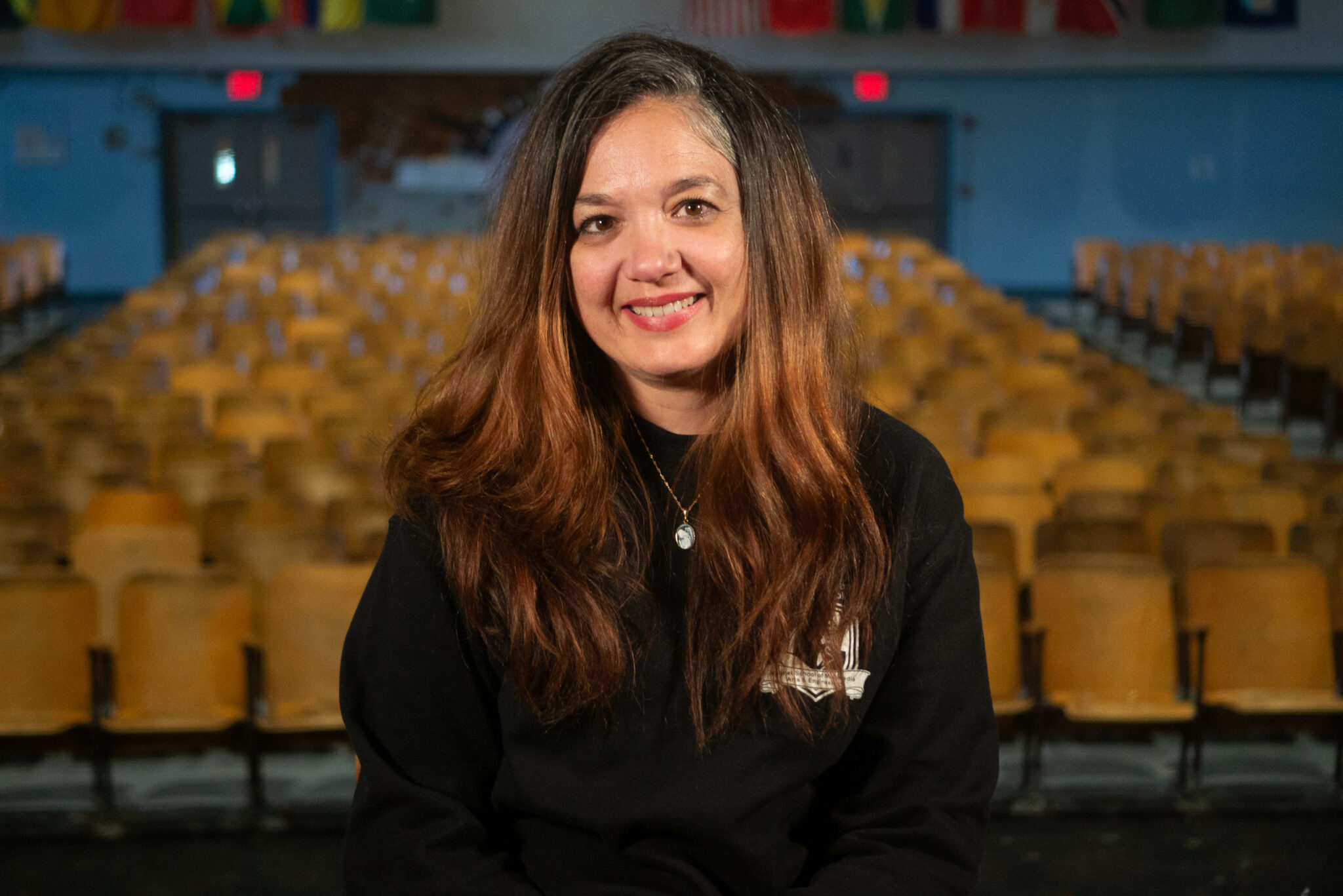 Angela Fraga smiling in school auditorium with empty seats behind her