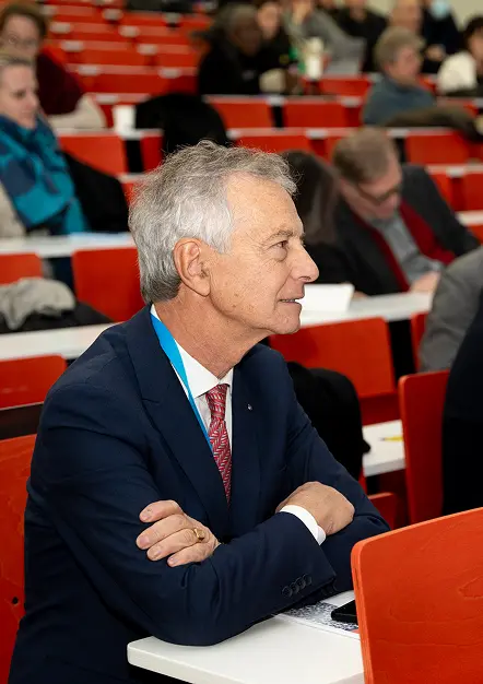 Un professionnel de la santé, assis dans les gradins lors d’un colloque ou d’un séminaire, écoute attentivement l’intervenant, illustrant l’engagement et la concentration des participants à la formation continue en santé.