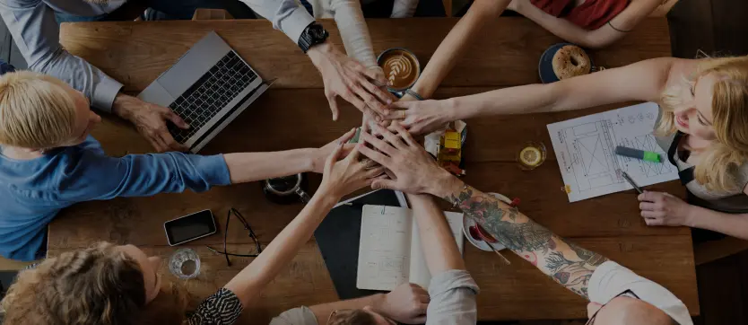 Vue de haut sur une équipe rassemblant ses mains au-dessus d’un bureau, geste symbolique de cohésion et de collaboration. Cette image souligne l’esprit d’équipe et la synergie au cœur de tout projet commun.