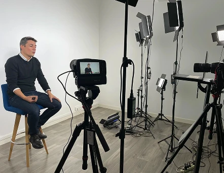 Un homme assis sur une chaise, entouré par plusieurs caméras et lumières orientées vers lui, illustre les coulisses d’un tournage professionnel et révèle l’ambiance technique et créative du plateau.