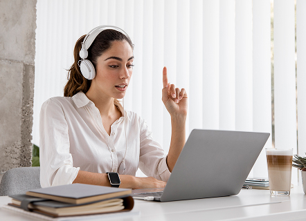 Femme devant son ordinateur, équipée d’un casque audio, qui lève le doigt pour intervenir lors d’un webinaire médical. L’image met en valeur l’utilisation d’outils adaptés pour la visioconférence et l’importance de l’interaction entre participants et intervenants dans le cadre de la formation et de l’échange en santé.