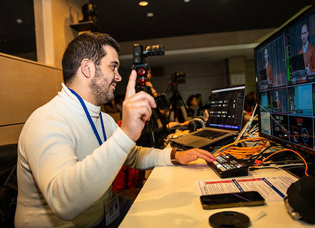 Homme devant une régie vidéo mobile, levant le doigt pour marquer le début d’un séminaire.