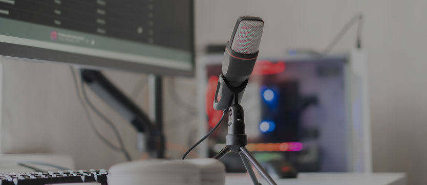 Studio d'enregistrement audio professionnel avec microphone sur trépied, casque et écran affichant une interface de mixage. En arrière-plan, un ordinateur équipé de LED colorées complète cet environnement technique dédié à la production sonore, au podcast et à la diffusion web.
