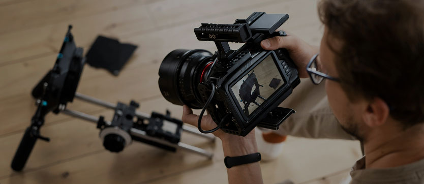 Un professionnel de la vidéo ajuste une caméra numérique haute définition, prêt à capturer des images pour une formation en santé. L’homme règle minutieusement l’appareil, posé au sol, à côté d’un accessoire essentiel de prise de vue. Cette scène illustre l’importance de la qualité vidéo dans la création de contenus pédagogiques numériques pour l’information et la formation en santé.