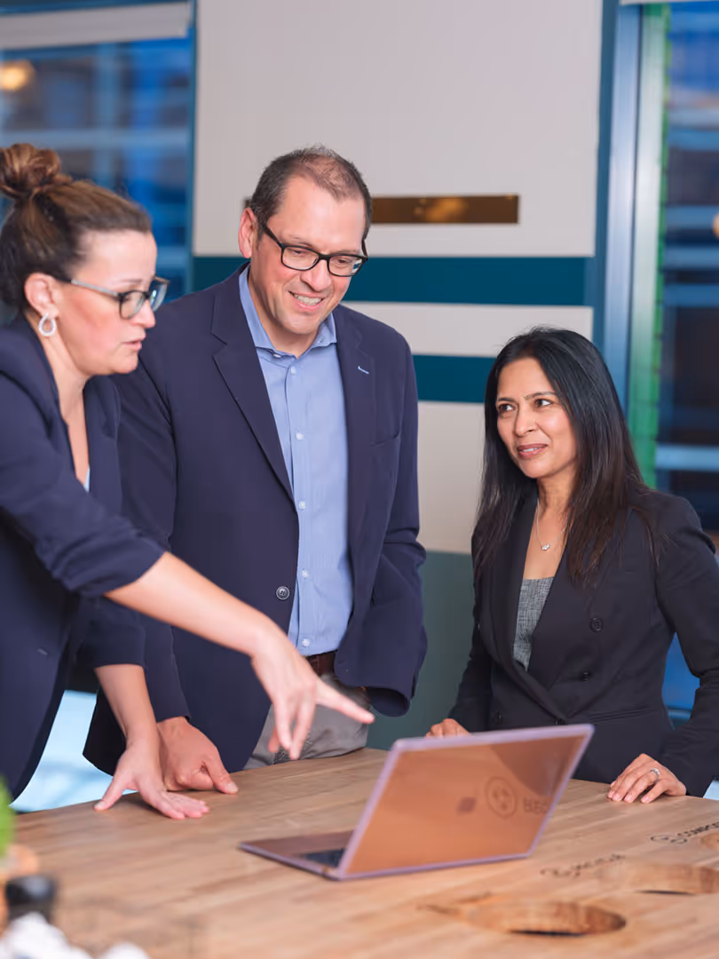 Three colleagues collaborating around a laptop during a team meeting in a modern office.