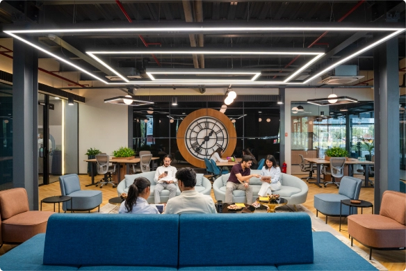 DevX Gift City modern office lounge with people working and a large clock on the back wall.