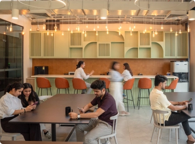 DevX Gift City modern office lounge with people sitting at tables and bar stools under hanging lights.