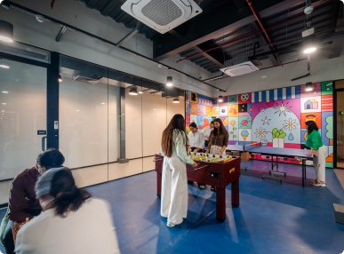 People playing foosball in a modern indoor recreational room with colorful wall art and ping pong table at DevX Gift City.