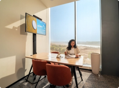 Woman sitting at a desk in a bright DevX Gift City office with two red chairs and a large window view.
