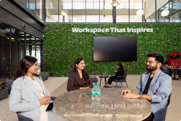 Three professionals talking at a round table in a modern DevX Gift City office with 'Workspace That Inspires' sign.