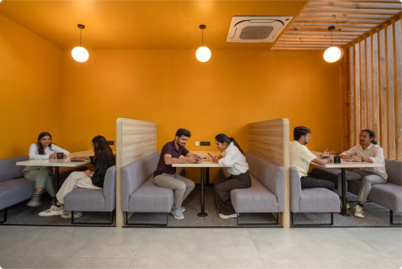 Three pairs of people sitting and talking in booth seating with an orange wall background at DevX Gift City.